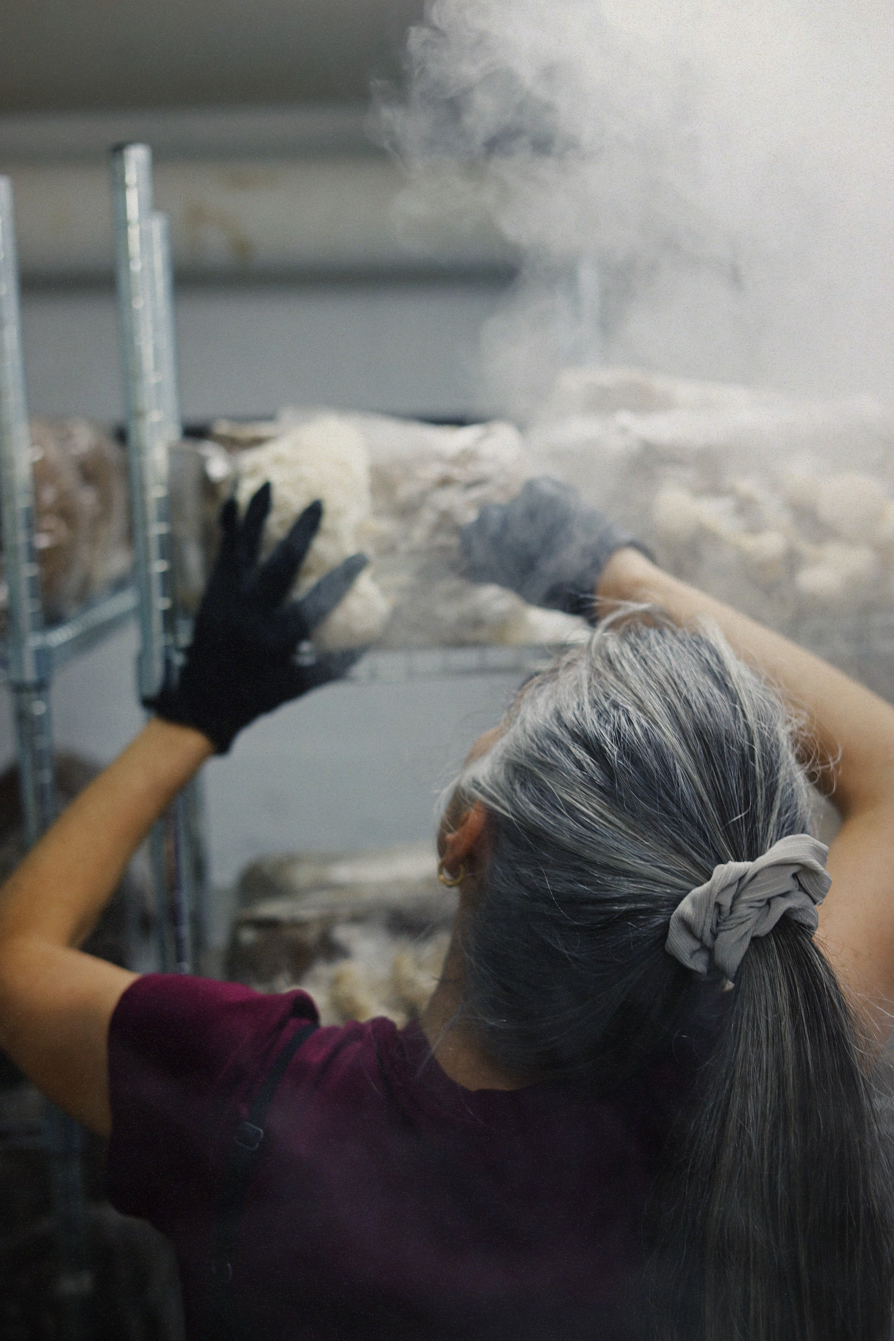 Person wearing gloves and a hairnet in a controlled environment with smoke and mushroom